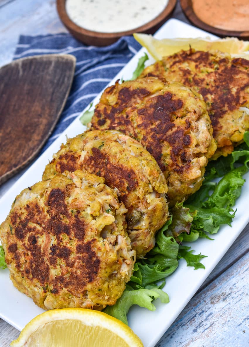 a row of cornbread stuffing crab cakes resting on green lettuce leaves on a white platter