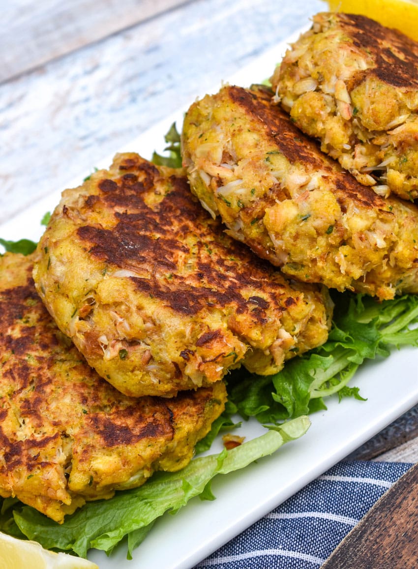 a row of cornbread stuffing crab cakes resting on green lettuce leaves on a white platter