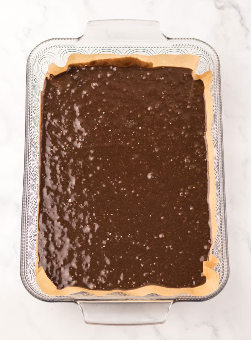 dr pepper brownie batter spread in an even layer in a parchment paper lined glass baking dish