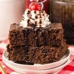 two dr pepper brownies topped with whipped cream and chocolate sauce stacked on a small white plate