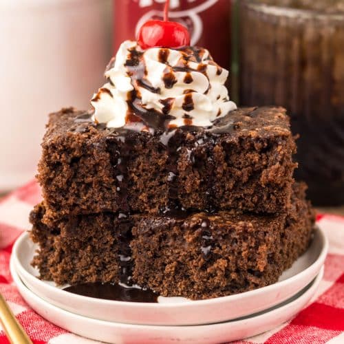 two dr pepper brownies topped with whipped cream and chocolate sauce stacked on a small white plate