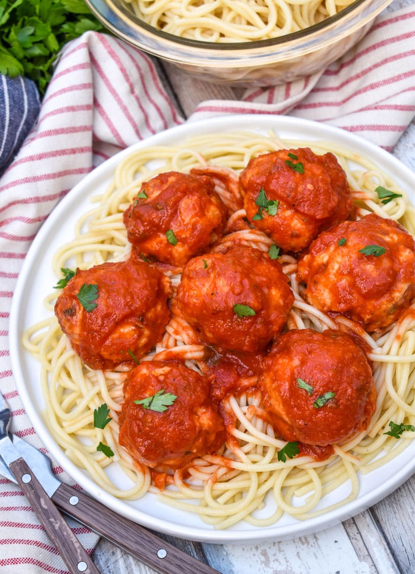 easy chicken meatballs coated in red sauce on a bed of cooked spaghetti on a white plate