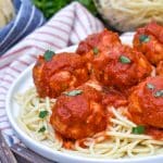 easy chicken meatballs coated in red sauce on a bed of cooked spaghetti on a white plate