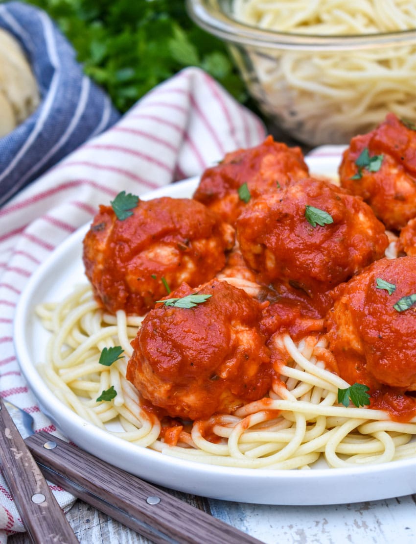 easy chicken meatballs coated in red sauce on a bed of cooked spaghetti on a white plate