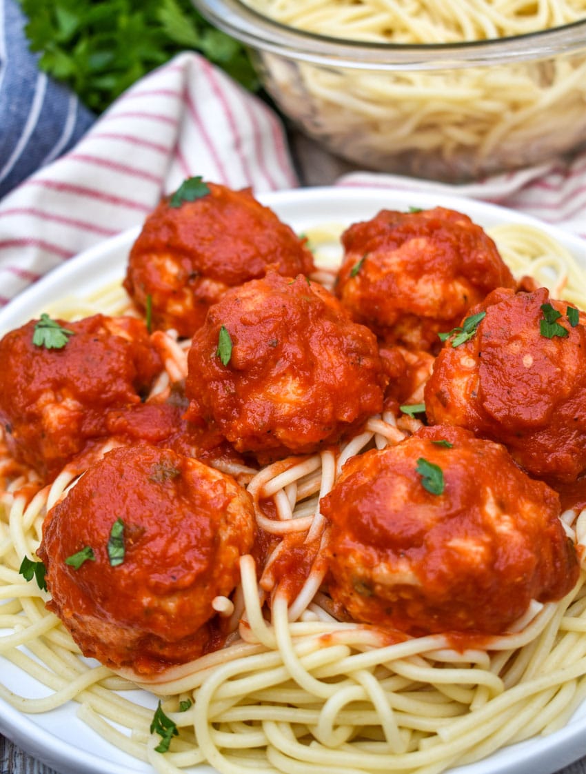 easy chicken meatballs coated in red sauce on a bed of cooked spaghetti on a white plate