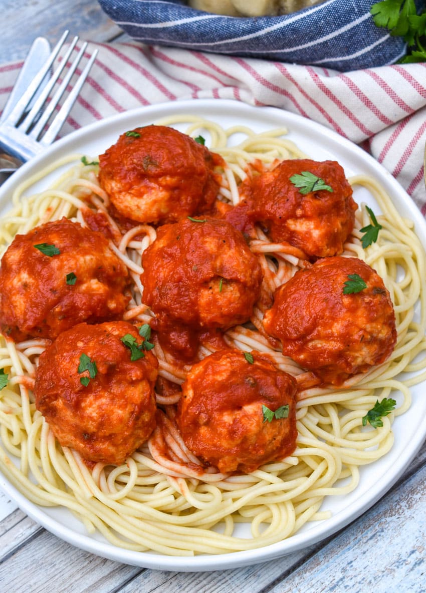 easy chicken meatballs coated in red sauce on a bed of cooked spaghetti on a white plate