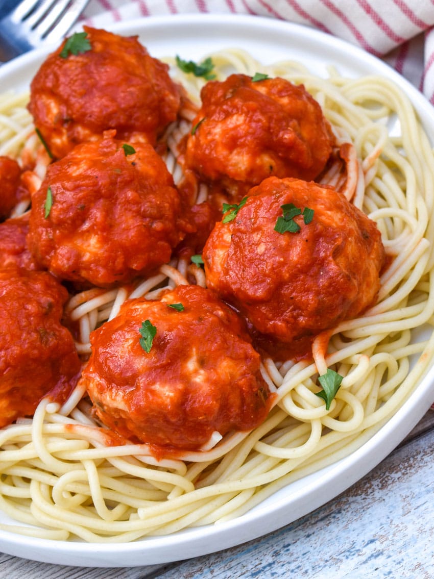 easy chicken meatballs coated in red sauce on a bed of cooked spaghetti on a white plate