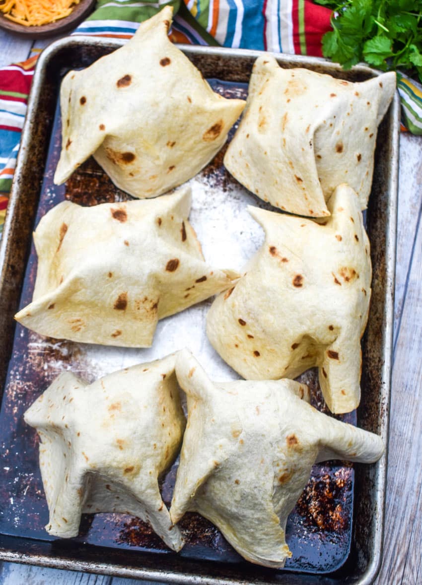 upside down homemade flour tortilla bowls arranged in two rows on a metal baking sheet