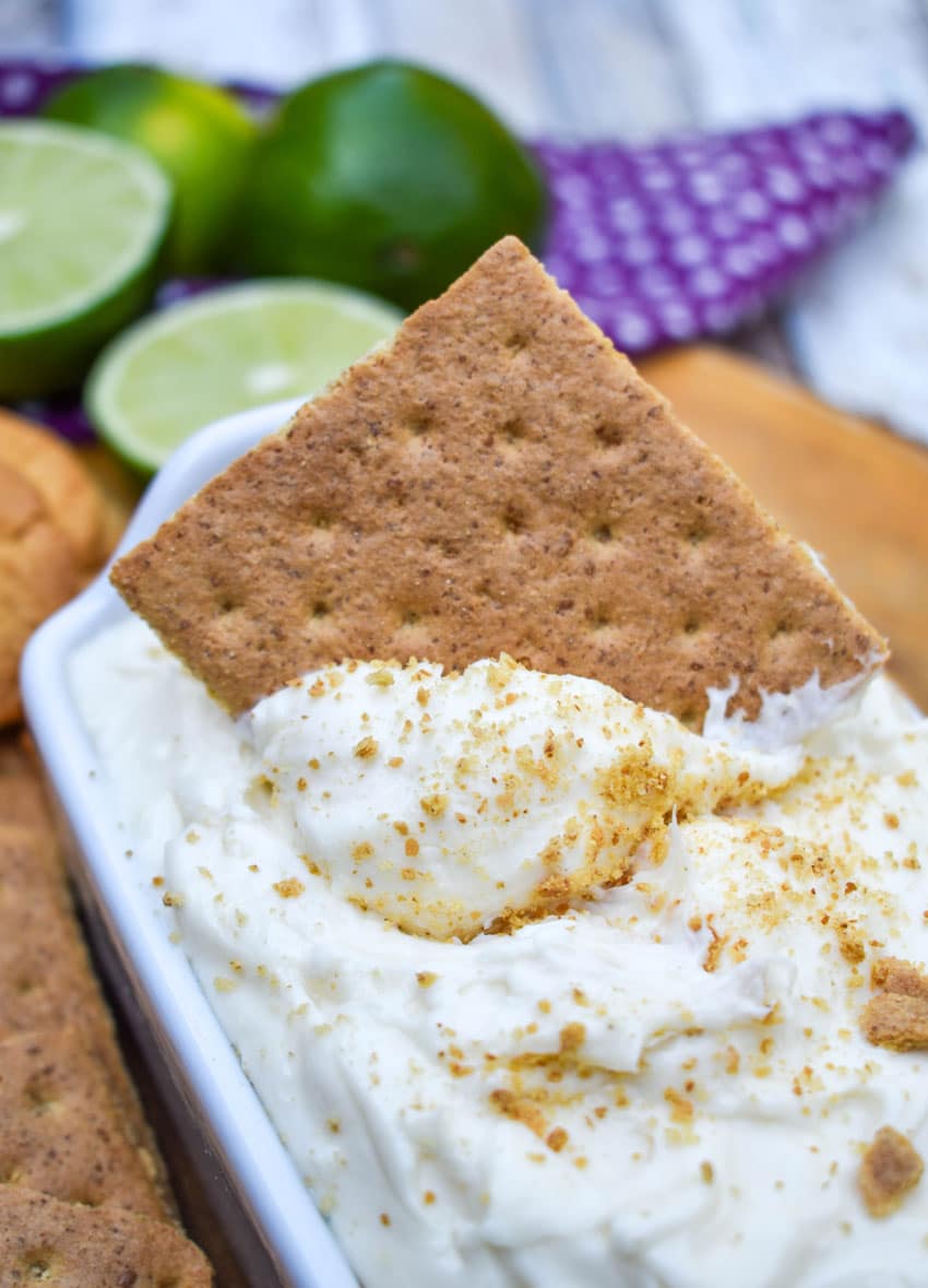a graham cracker scooping key lime pie dip out of a small white serving dish