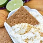 a graham cracker scooping key lime pie dip out of a small white serving dish