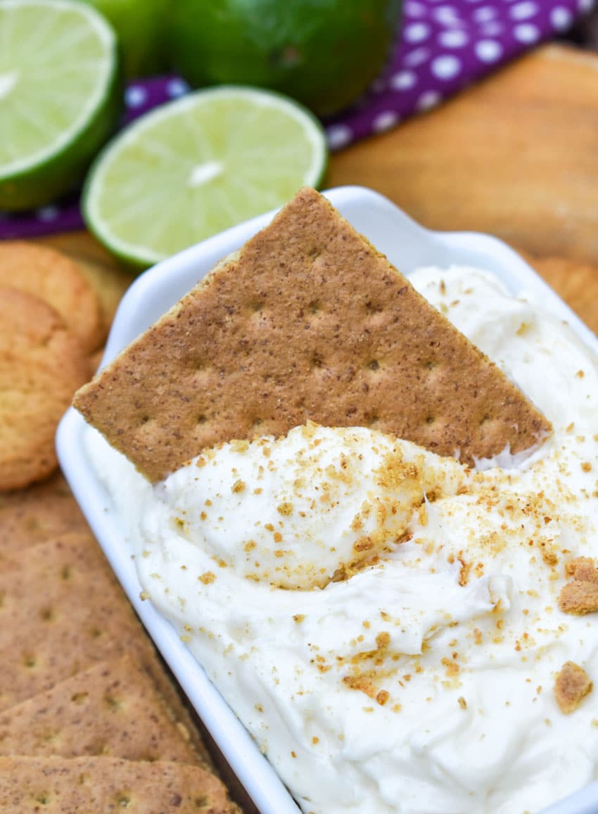 a graham cracker scooping key lime pie dip out of a small white serving dish