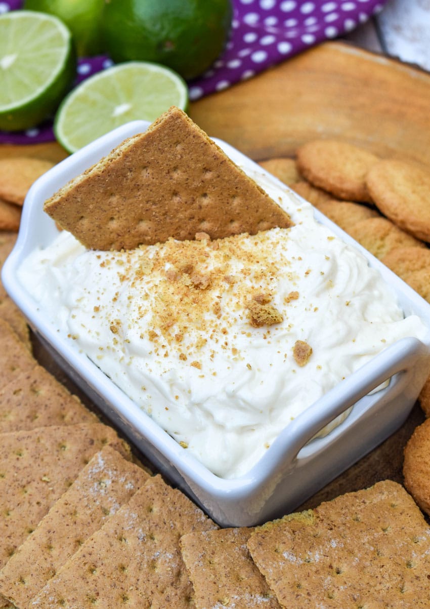 a graham cracker scooping key lime pie dip out of a small white serving dish