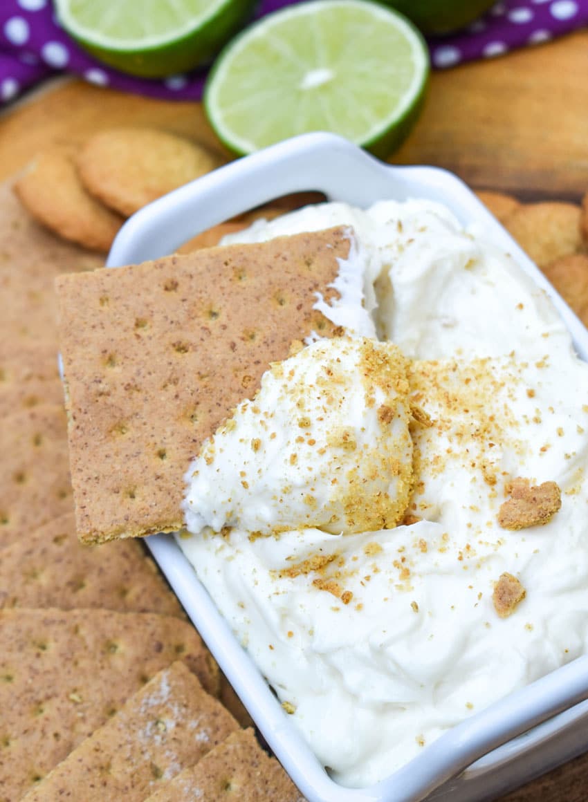 a graham cracker scooping key lime pie dip out of a small white serving dish