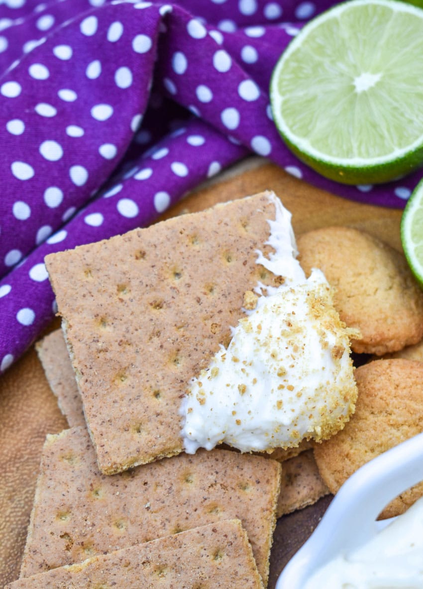 a key lime pie dip topped graham cracker resting on a wooden cutting board