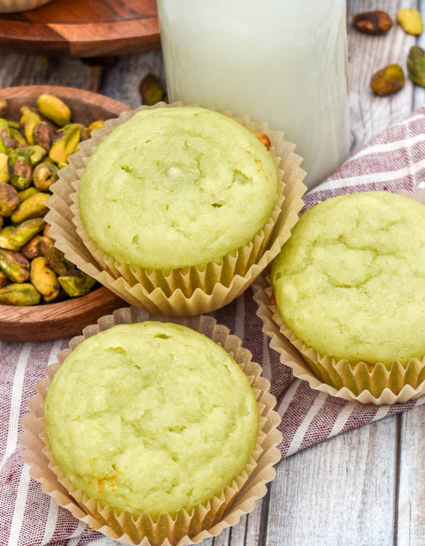 three pistachio pudding muffins on a wooden table with a glass of milk in the background