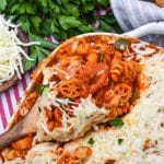 a wooden spoon scooping homemade cavatini pasta supreme out of a white baking dish