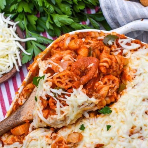 a wooden spoon scooping homemade cavatini pasta supreme out of a white baking dish