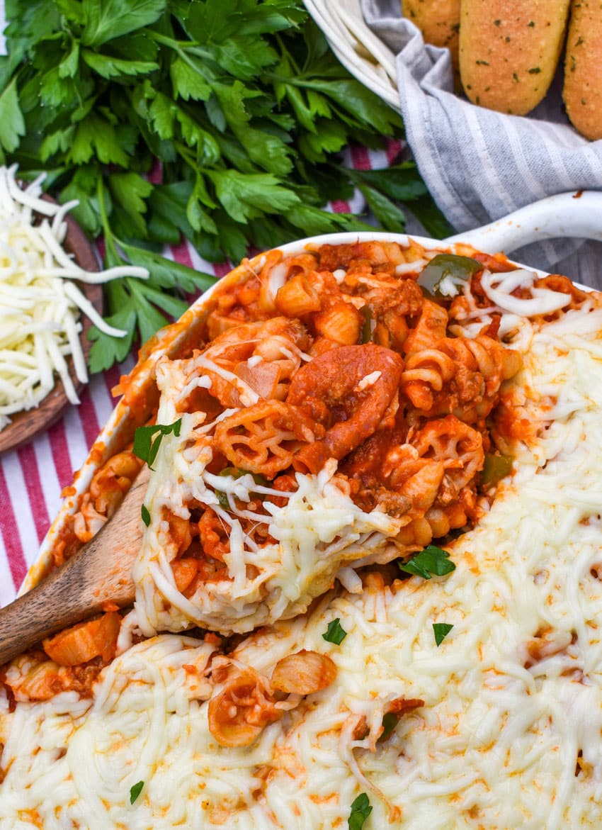 a wooden spoon scooping homemade cavatini pasta supreme out of a white baking dish