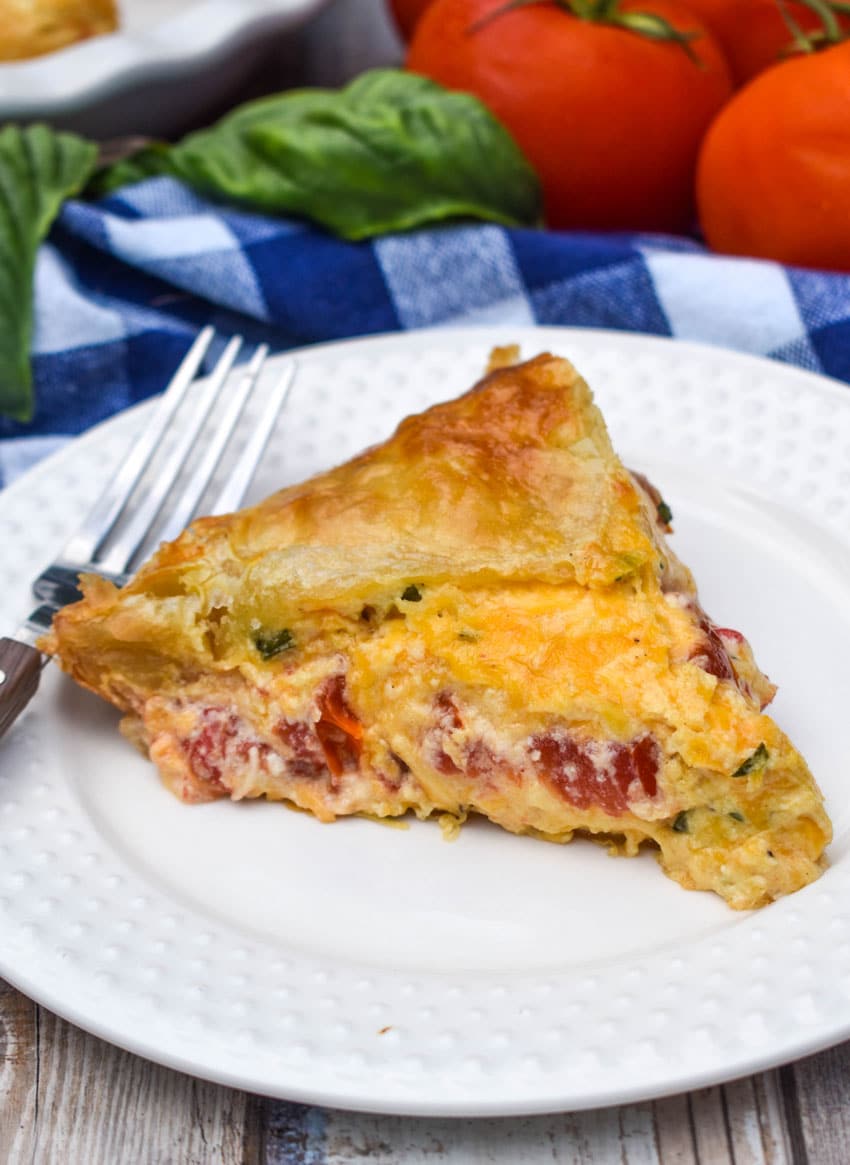 a slice of tomato pie with puff pastry crust on a small white plate with a fork resting on the side