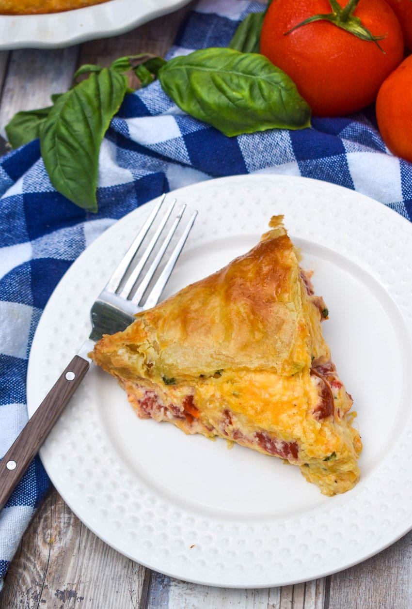 a slice of tomato pie with puff pastry crust on a small white plate with a fork resting on the side
