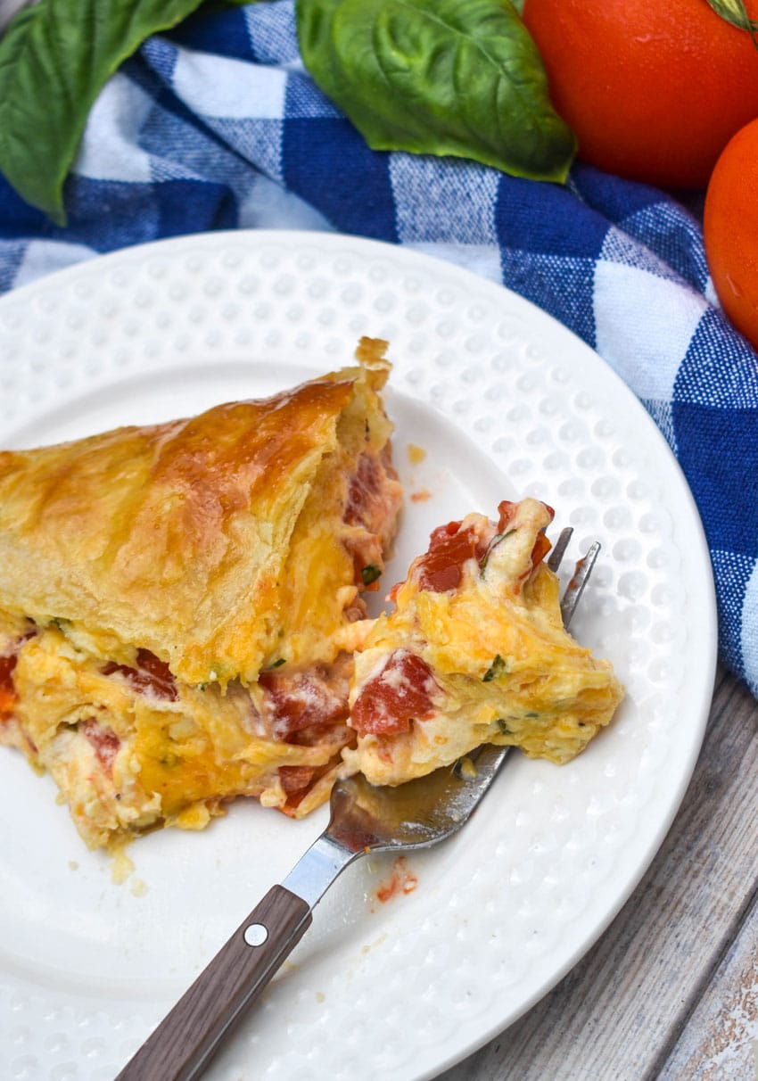 a slice of tomato pie with puff pastry crust on a small white plate with a fork resting on the side
