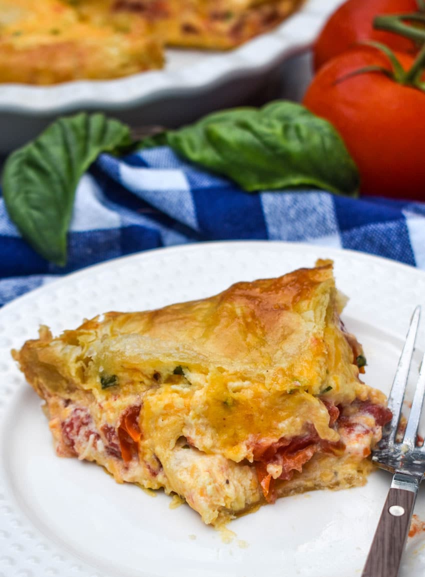 a slice of tomato pie with puff pastry crust on a small white plate with a fork resting on the side