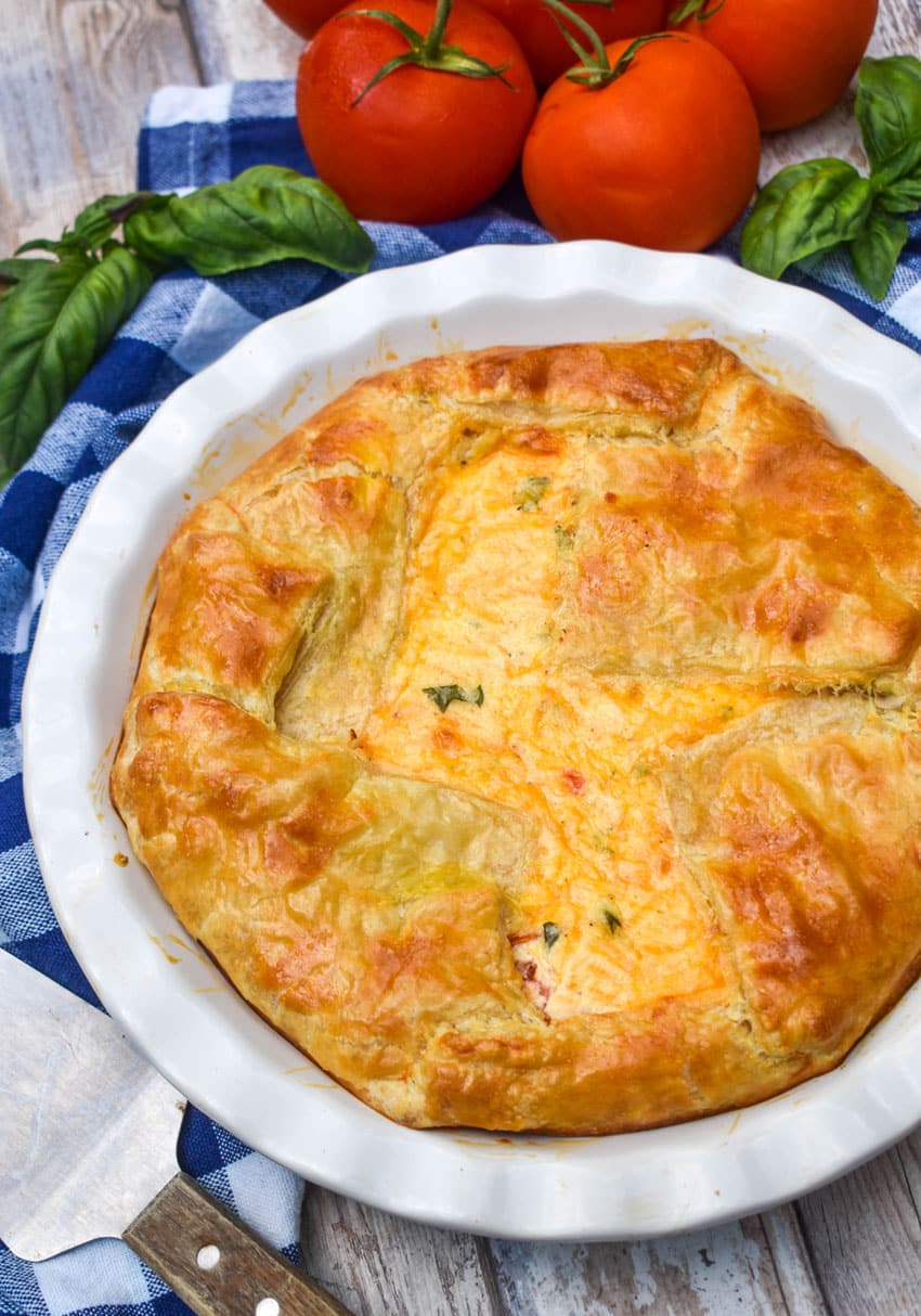 a tomato pie with puff pastry crust in a white pie dish