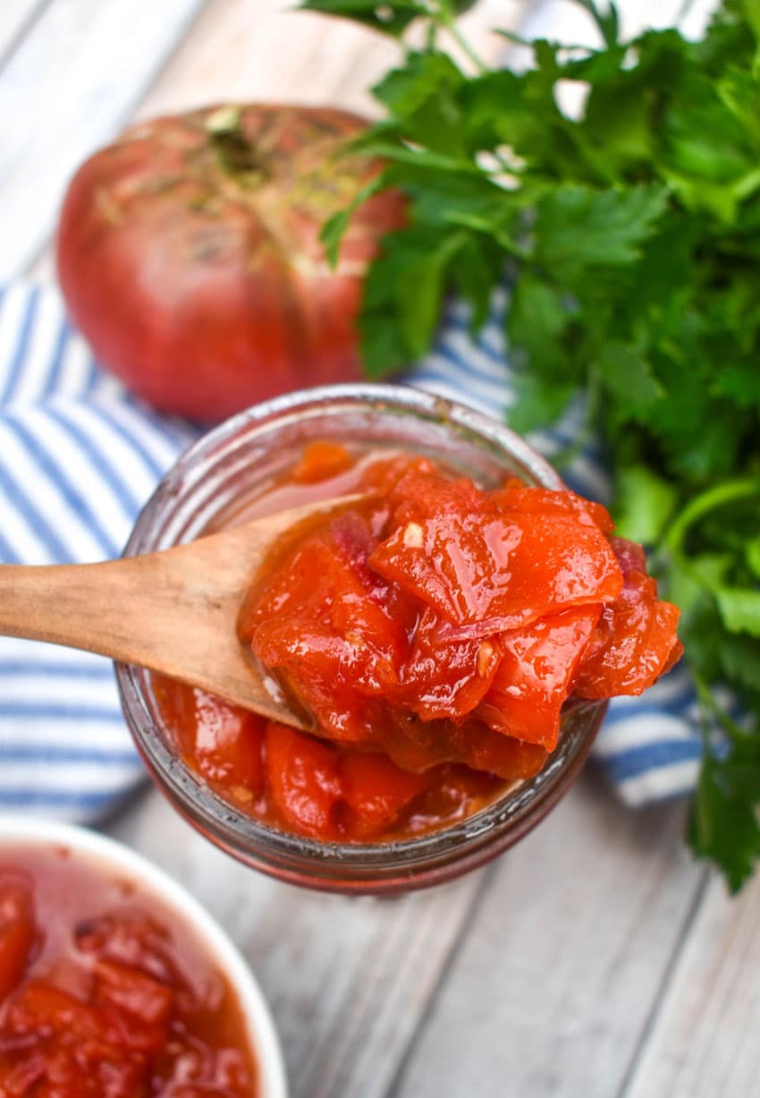 a wooden spoon scooping homemade tomato relish out of a small glass jar