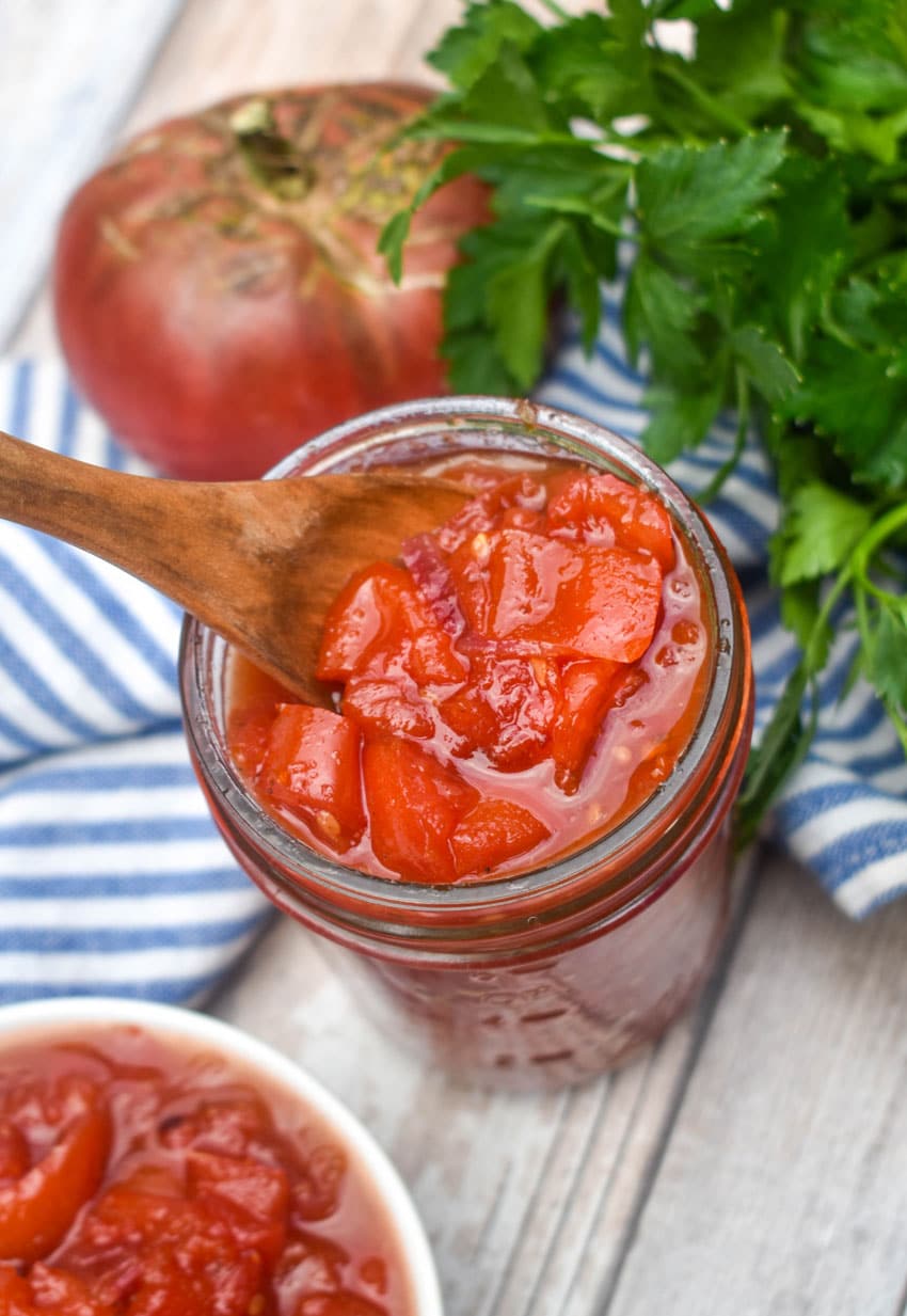 a wooden spoon scooping homemade tomato relish out of a small glass jar