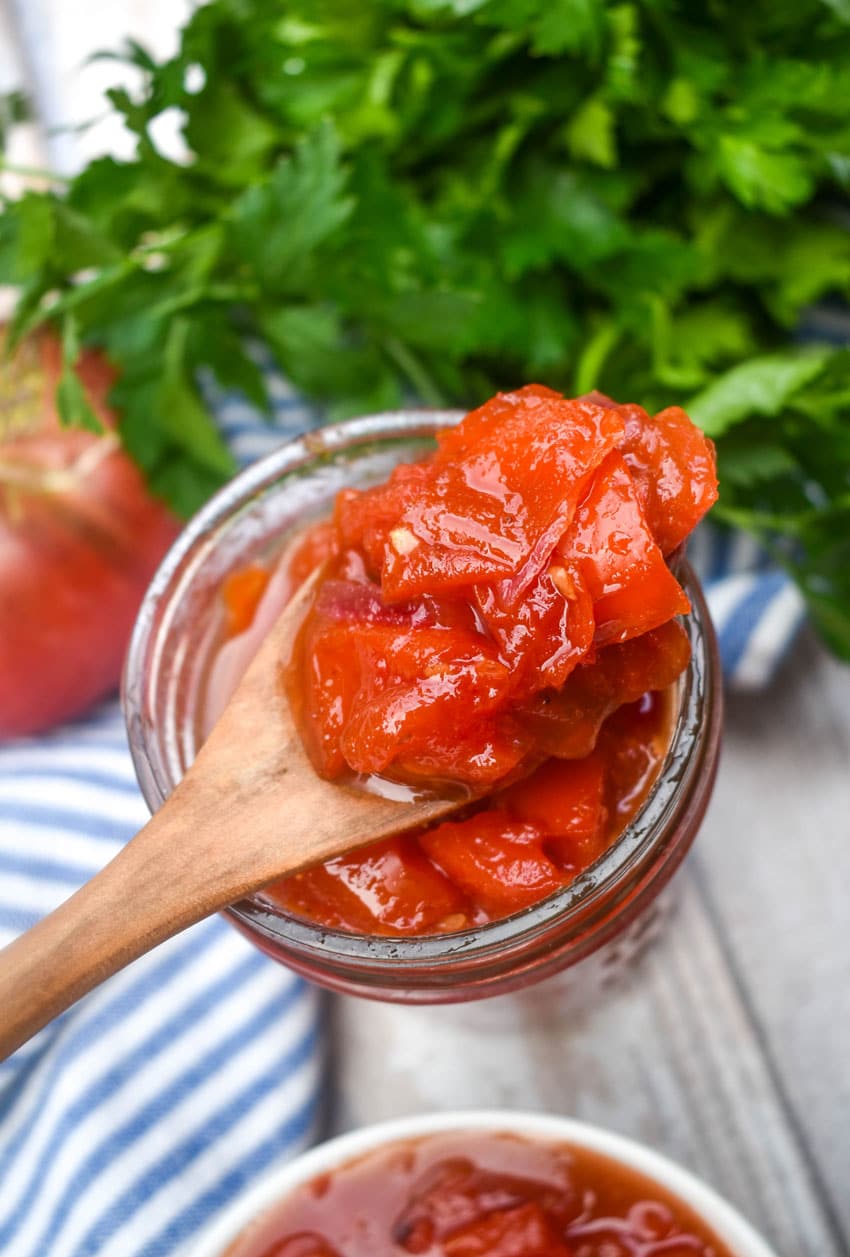 a wooden spoon scooping homemade tomato relish out of a small glass jar