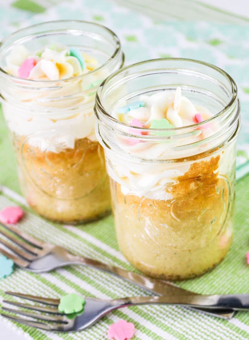 two single serve cakes topped with swirls of white frosting in small glass jars