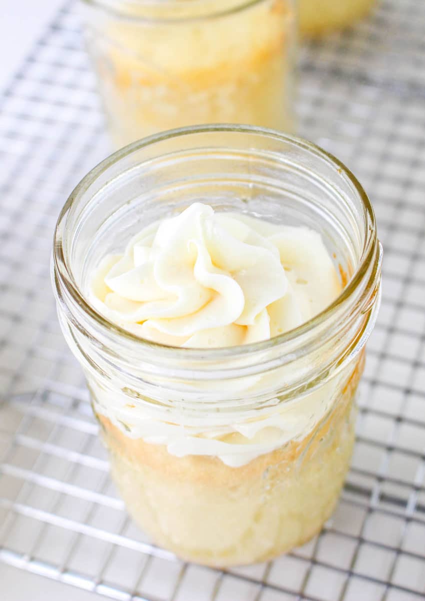 frosted baked mini cakes in jars resting on a metal cooling rack
