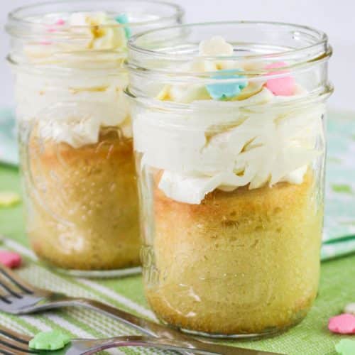 two single serve cakes topped with swirls of white frosting in small glass jars