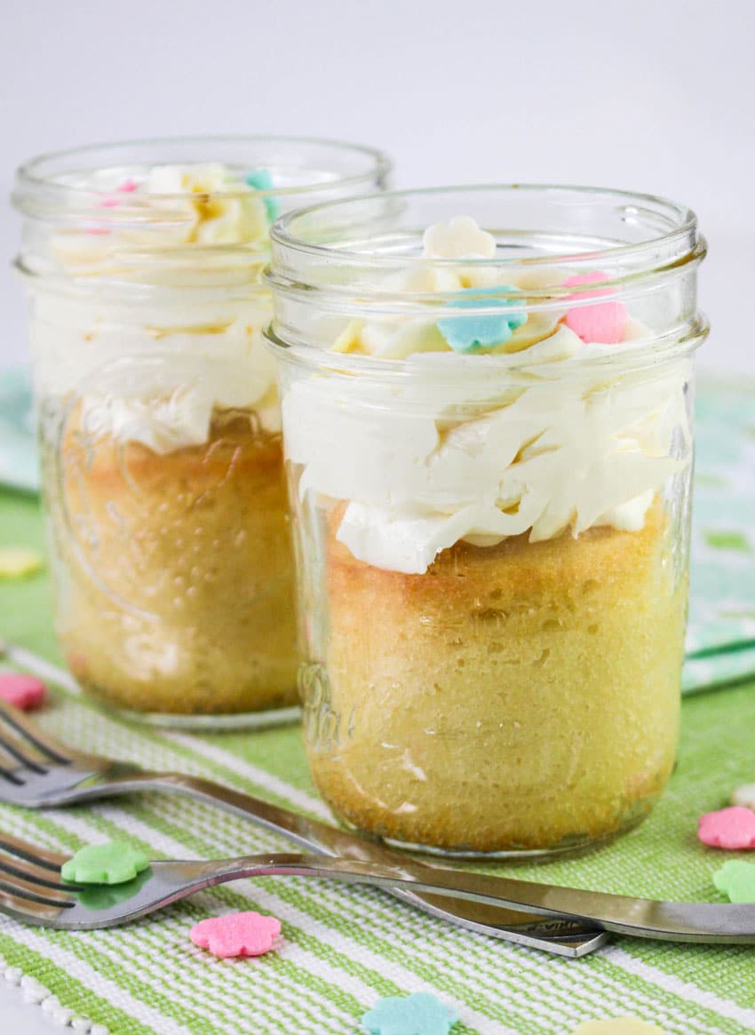 two single serve cakes topped with swirls of white frosting in small glass jars