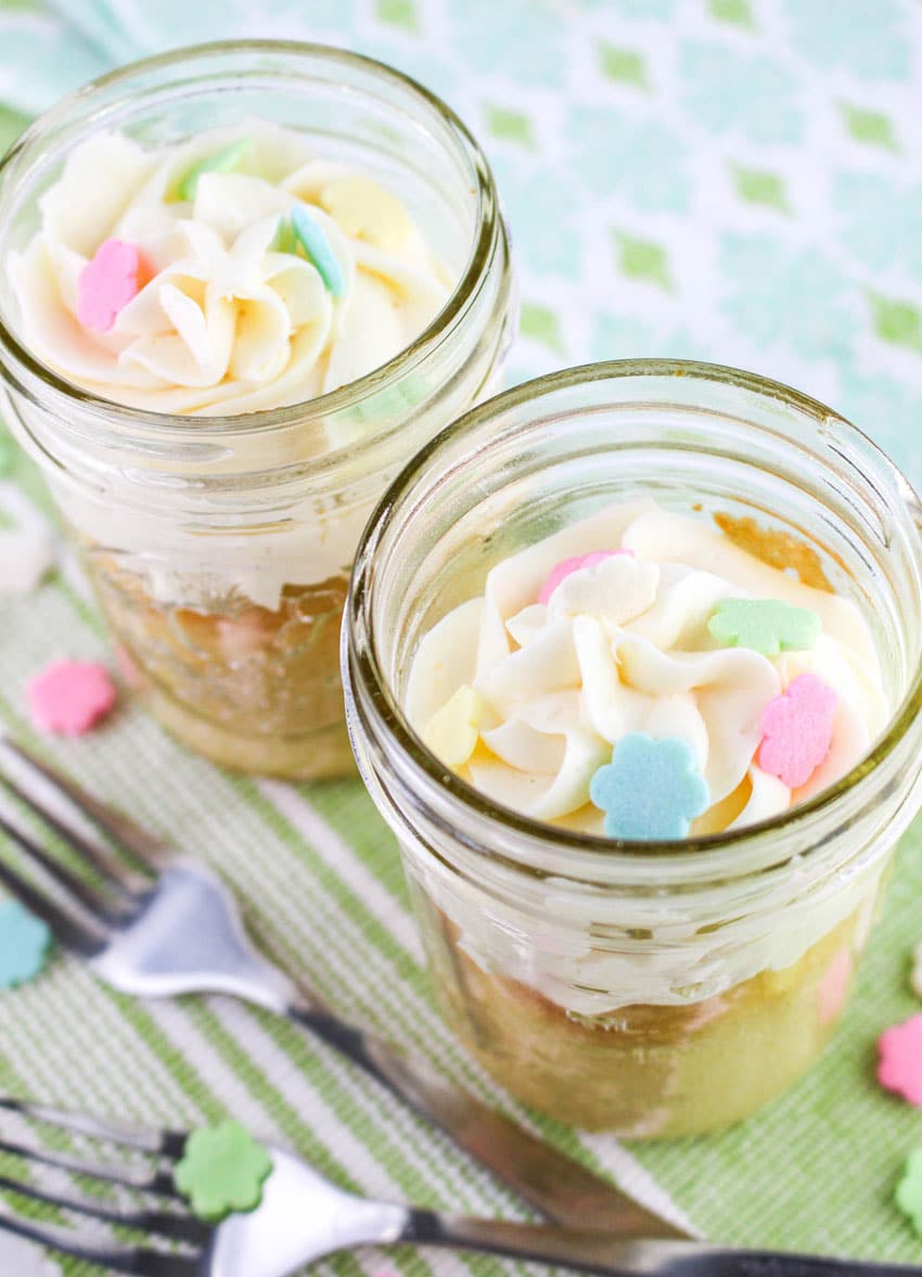 two single serve cakes topped with swirls of white frosting in small glass jars