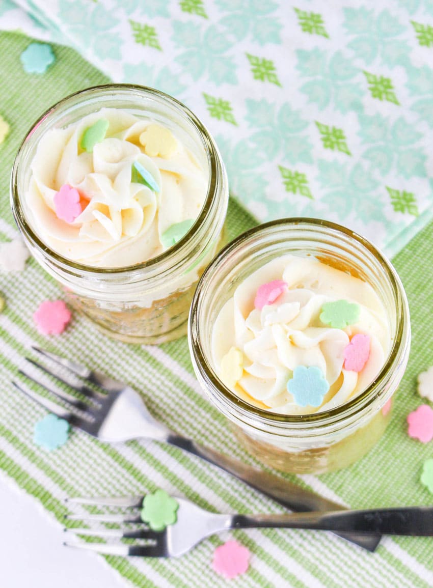 two single serve cakes topped with swirls of white frosting in small glass jars