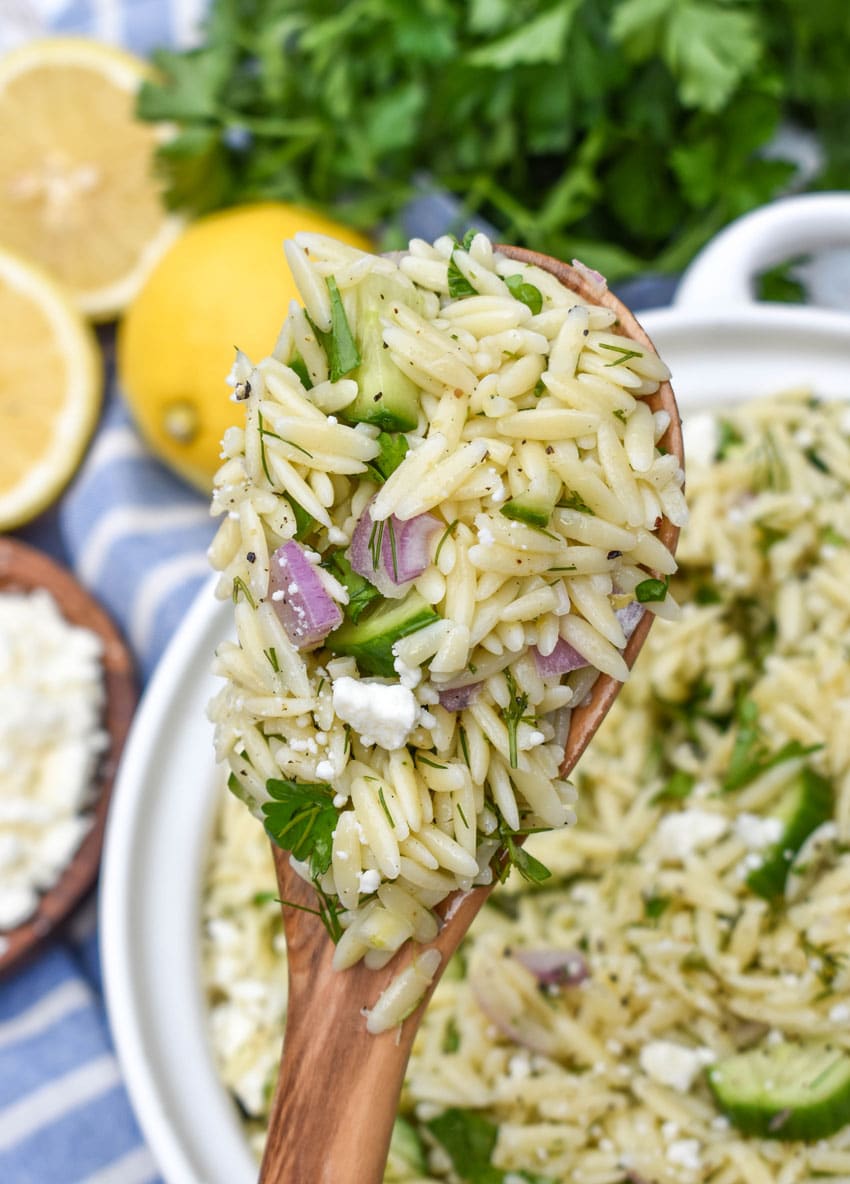 a wooden spoon holding up a scoop of cucumber lemon orzo pasta salad