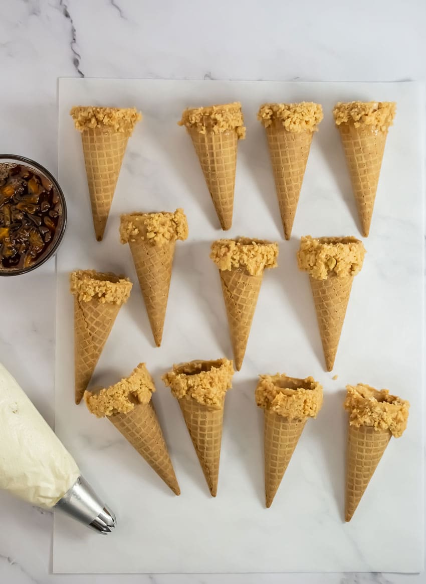 cookie crumb coated ice cream cones arranged in rows on a piece of white parchment paper