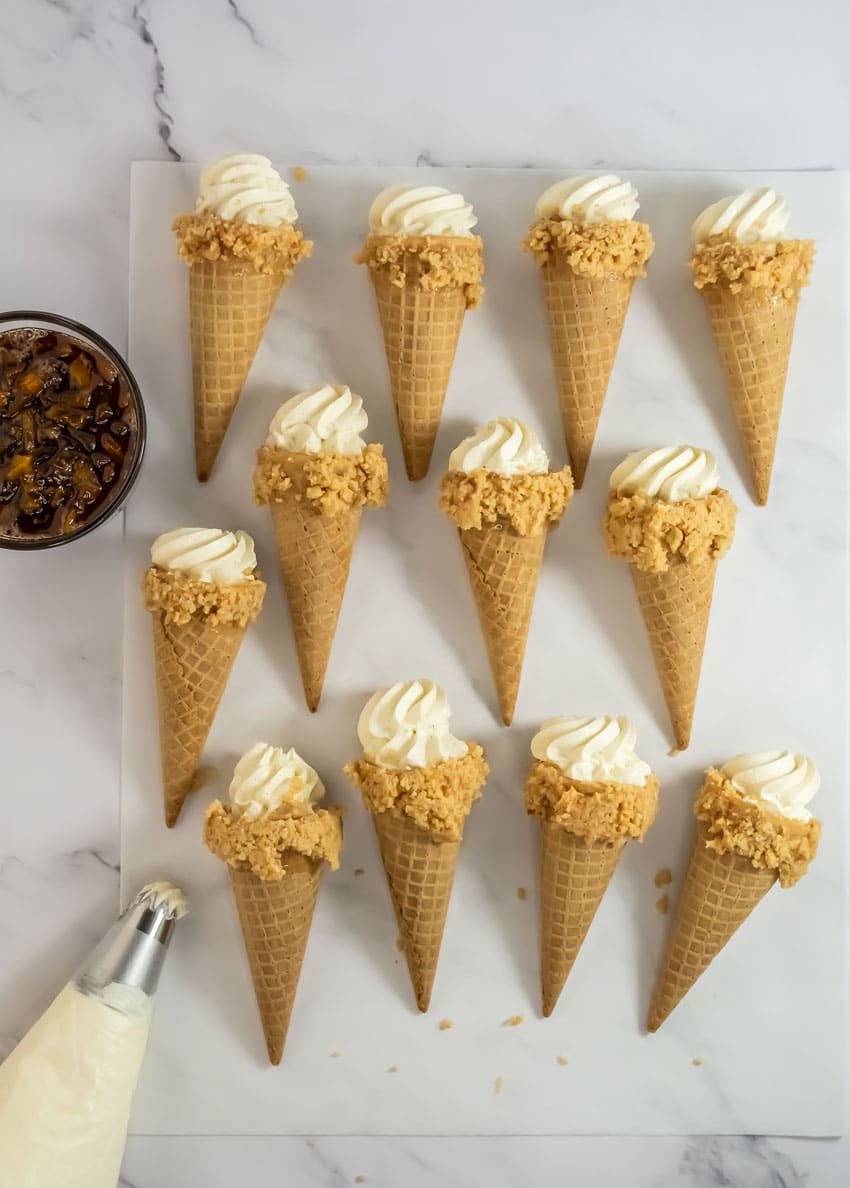 peach cobbler cheesecake cones arranged in rows on white parchment paper
