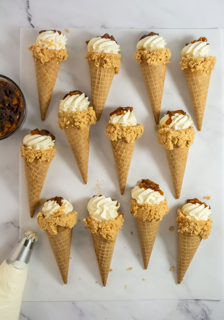 peach cobbler cheesecake cones arranged in rows on white parchment paper