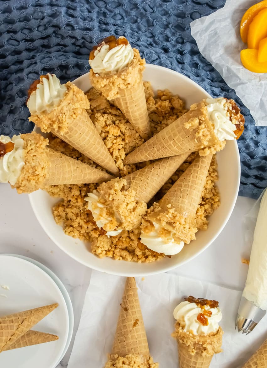 peach cobbler cheesecake cones arranged in a row on white parchment paper