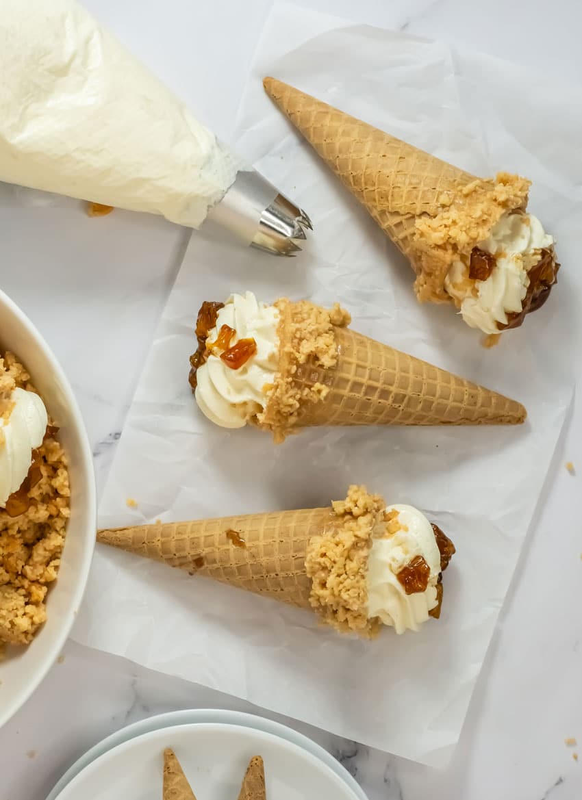 peach cobbler cheesecake cones arranged in a row on white parchment paper
