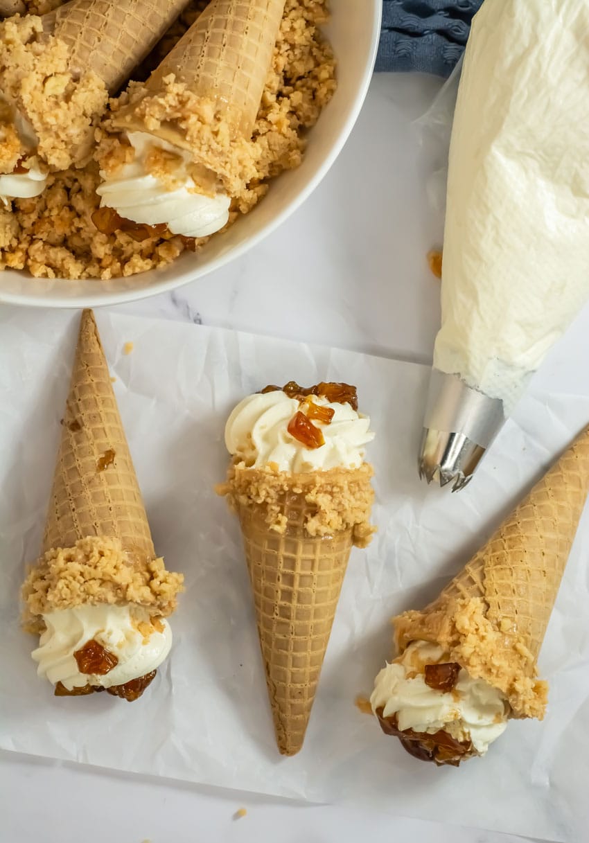 peach cobbler cheesecake cones arranged in a row on white parchment paper