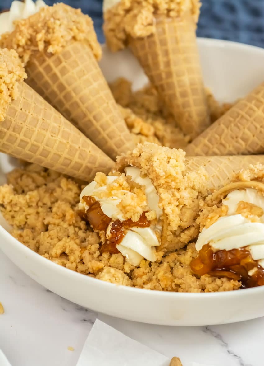 peach cobbler cheesecake cones arranged in a row on white parchment paper