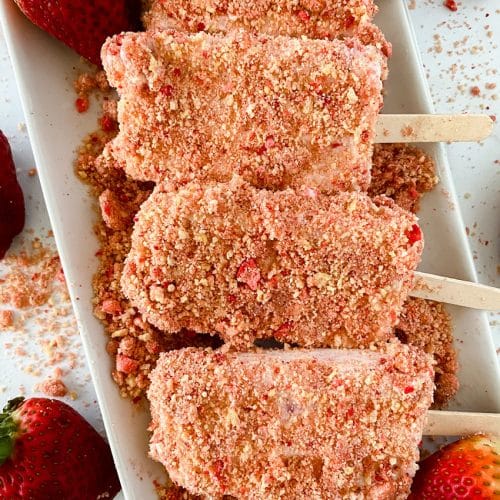 homemade strawberry crunch ice cream bars arranged in a row on a white serving platter