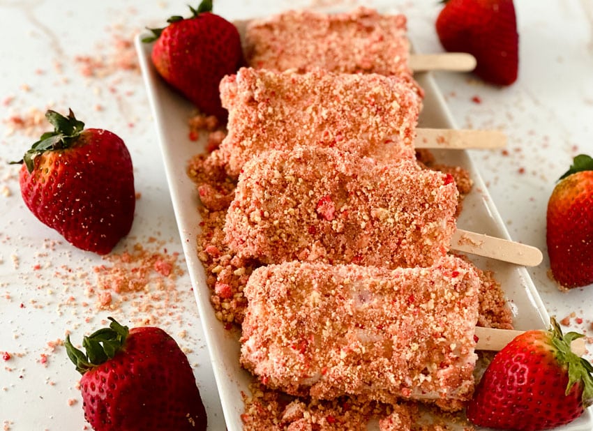 homemade strawberry crunch ice cream bars arranged in a row on a white serving platter