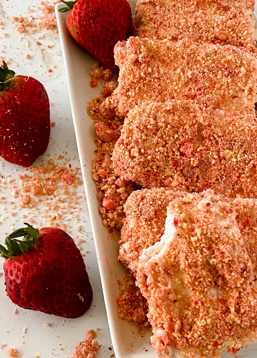 homemade strawberry ice cream popsicles laying on strawberry crunch topping on a white platter
