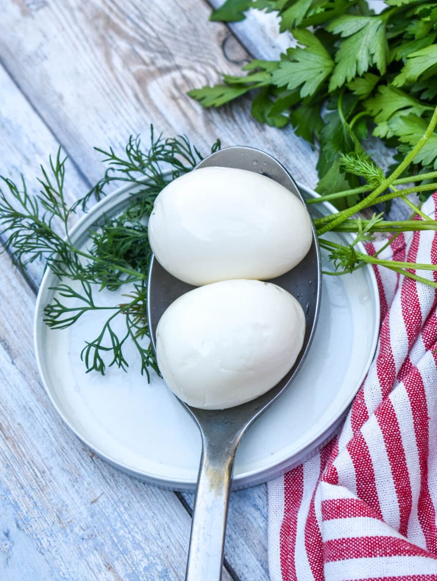 two easy homemade pickled eggs resting on a metal spoon next to fresh dill weed