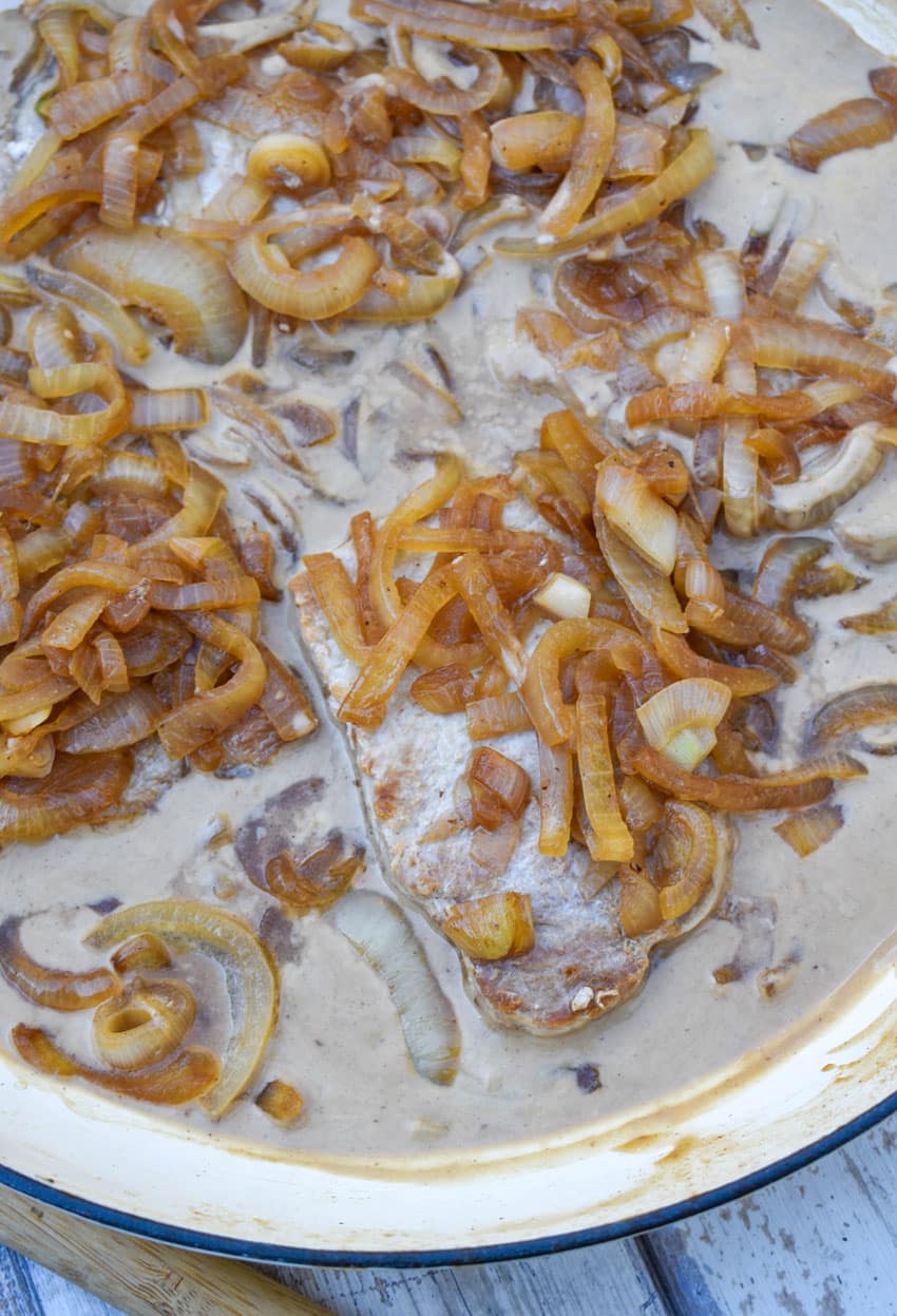 pork chops in cream sauce with caramelized onions in a large enameled cast iron skillet