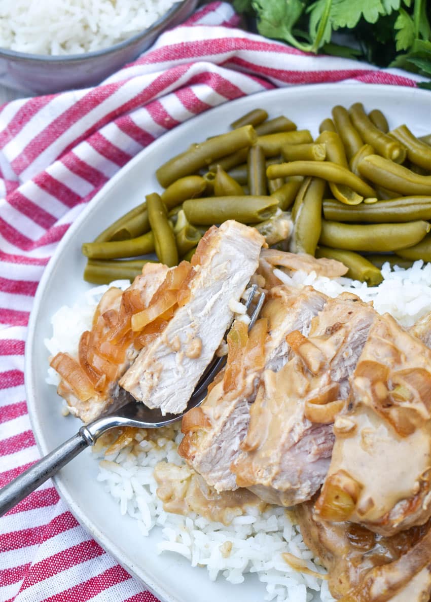pork chops with cream sauce and onions over steamed white rice next to green beans on a white dinner plate
